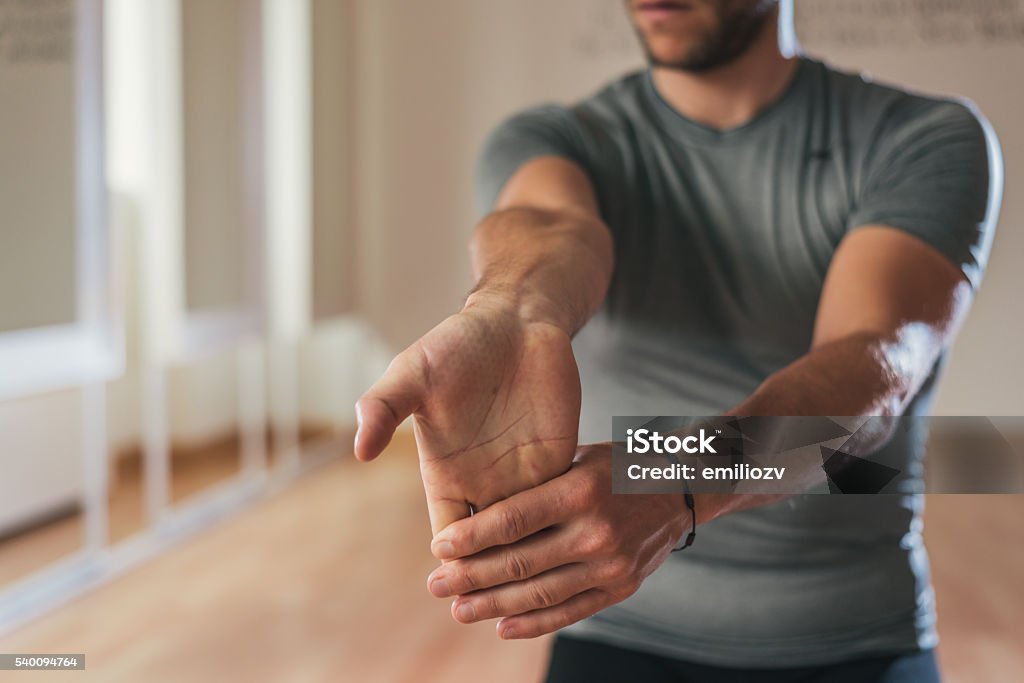 Sporty man stretching forearm before gym workout. Fitness strong male athlete standing indoor warming up.