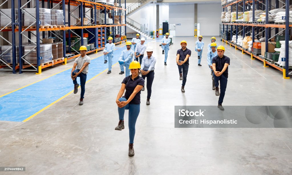 Happy group of Latin American workers at a factory doing stretching exercises while taking a break - healthy lifestyle concepts